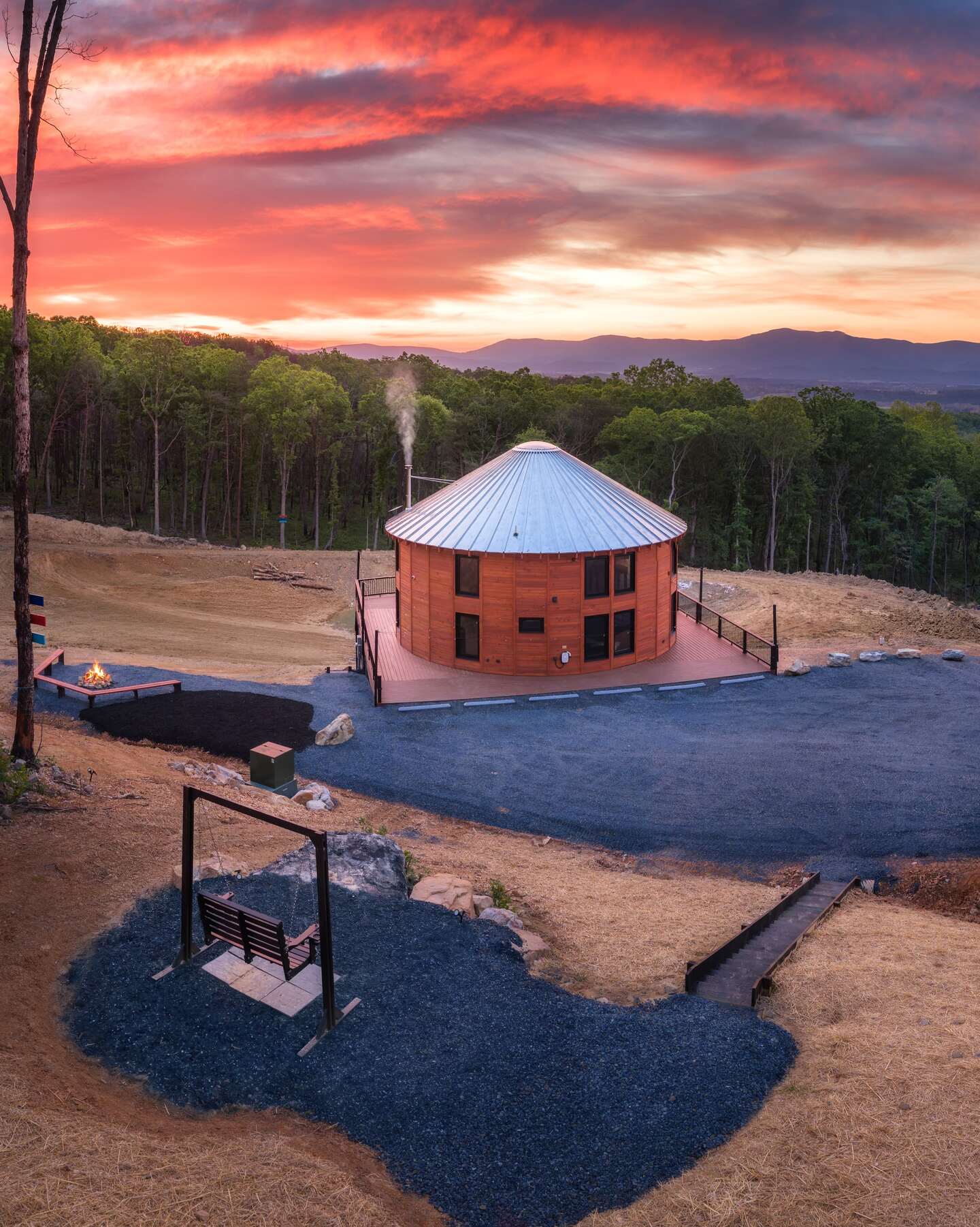 The round building on its bare site at sunset, metal roof and larch siding